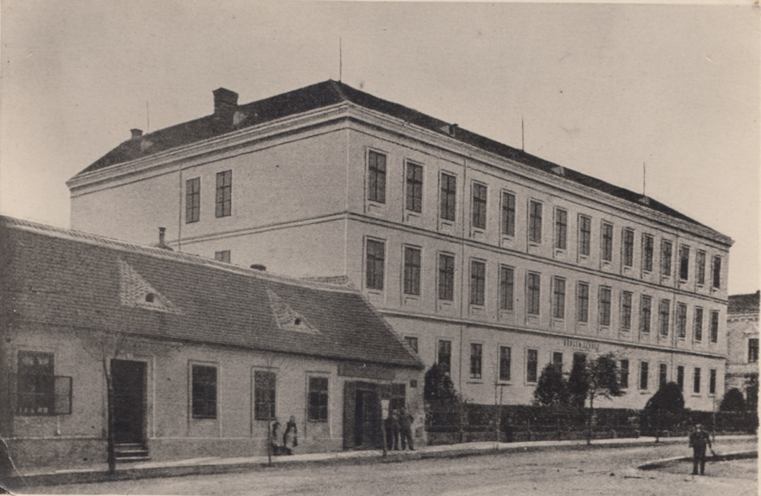 Links neben dem 1873 errichteten Schulgebäude in der Bahnstraße (heute Teil des Gebäudekomplexes der Mittelschulen) das alte bis ca. 1904 bestehende Gebäude mit der für ein Eckhaus üblichen Doppeladresse Bahnstraße 1/Mitschastraße 2